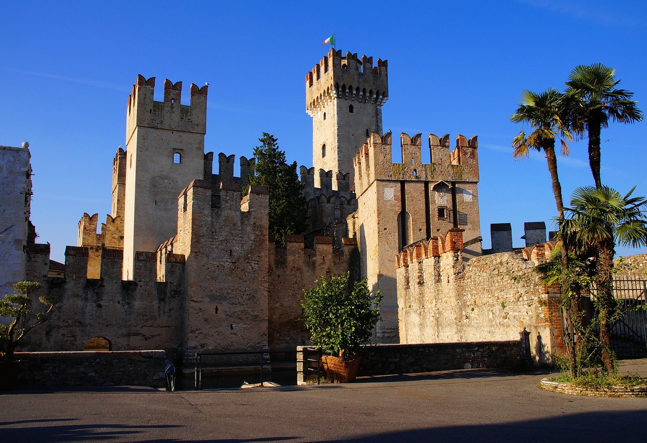 Castello medievale italiano con torri e mura imponenti, immerso in un paesaggio pittoresco.