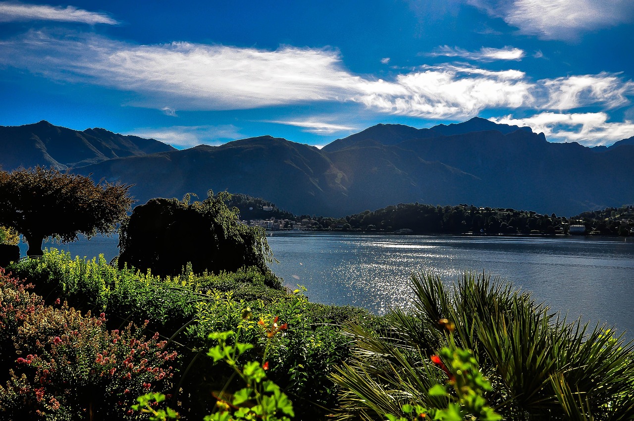 Vista panoramica del lago di Como con montagne sullo sfondo e cielo sereno.