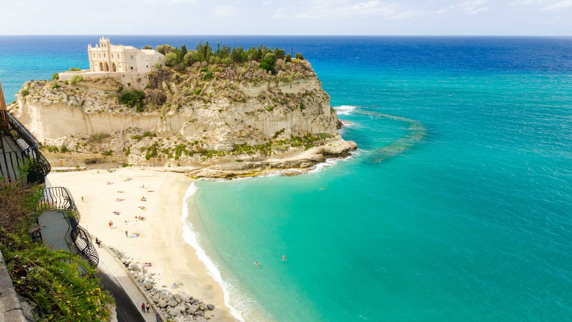 Spiaggia di sabbia bianca in Sicilia, con acque cristalline e scogliere sullo sfondo.