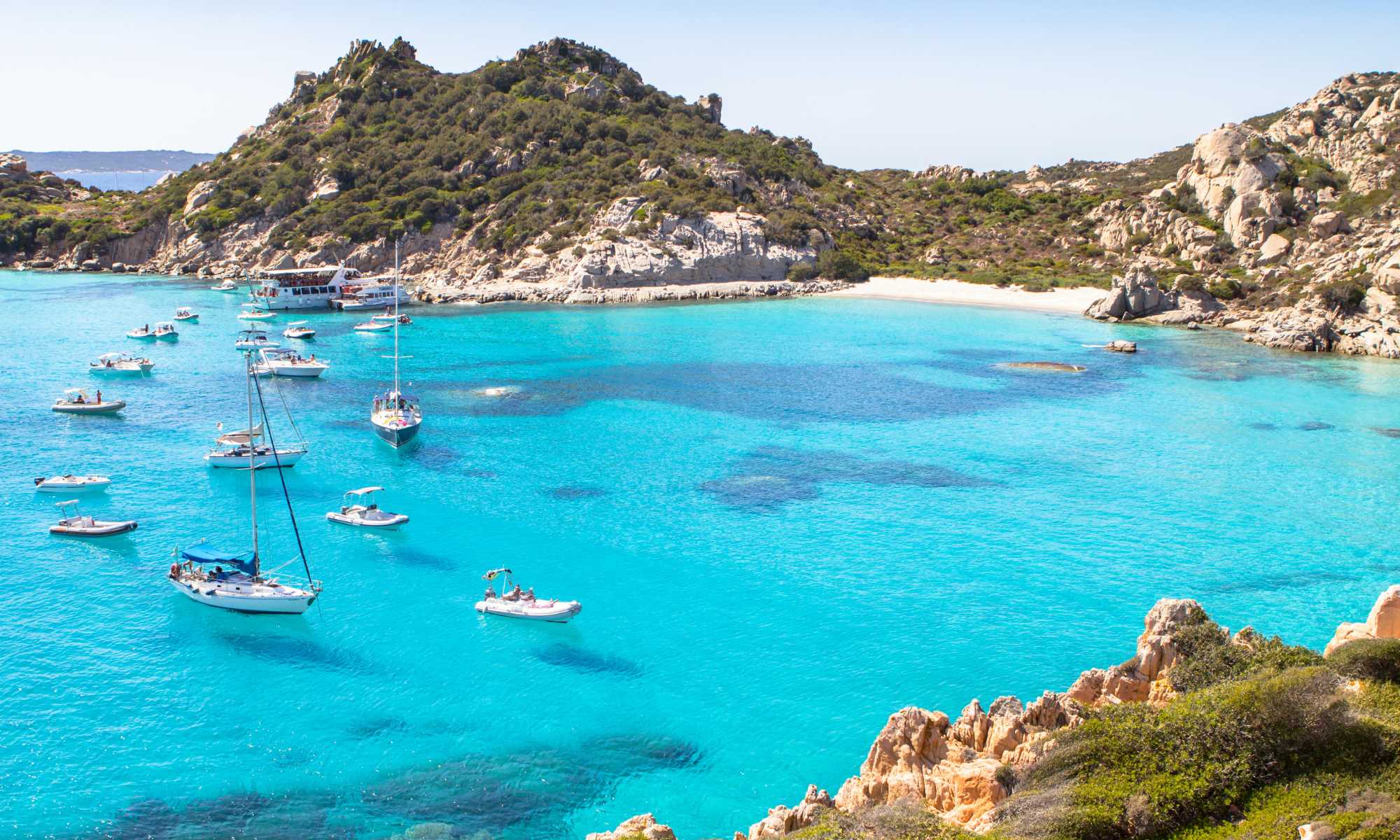 Caletta cristallina in Sardegna, circondata da rocce e vegetazione lussureggiante. Un vero paradiso nascosto.